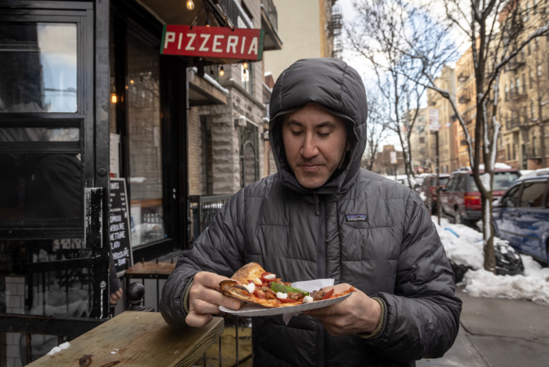 Michael Solomonov stands eating pizza in front of L'industrie in Brooklyn.