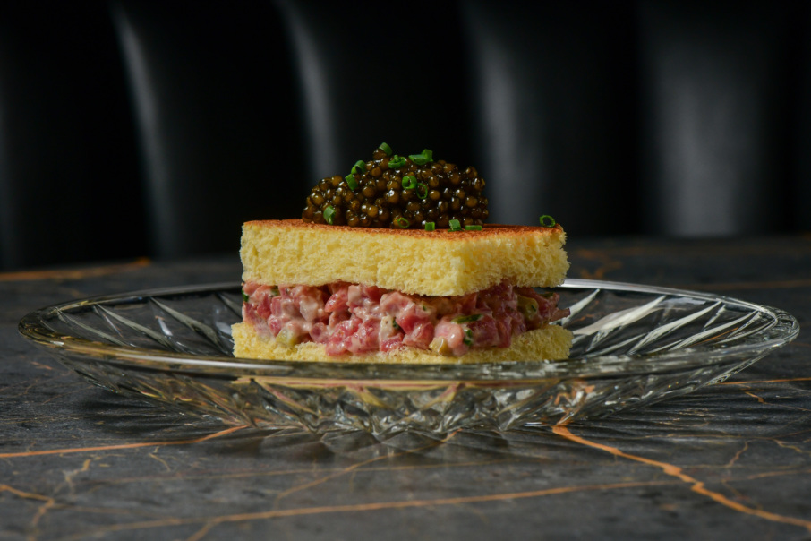 The steak tartare features Wagyu steak, truffle oil, caviar, and chives, and is assembled like a sandwich with a brioche bun.