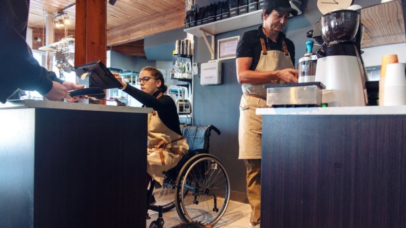 Woman in wheelchair works enters order into POS system in coffee shop