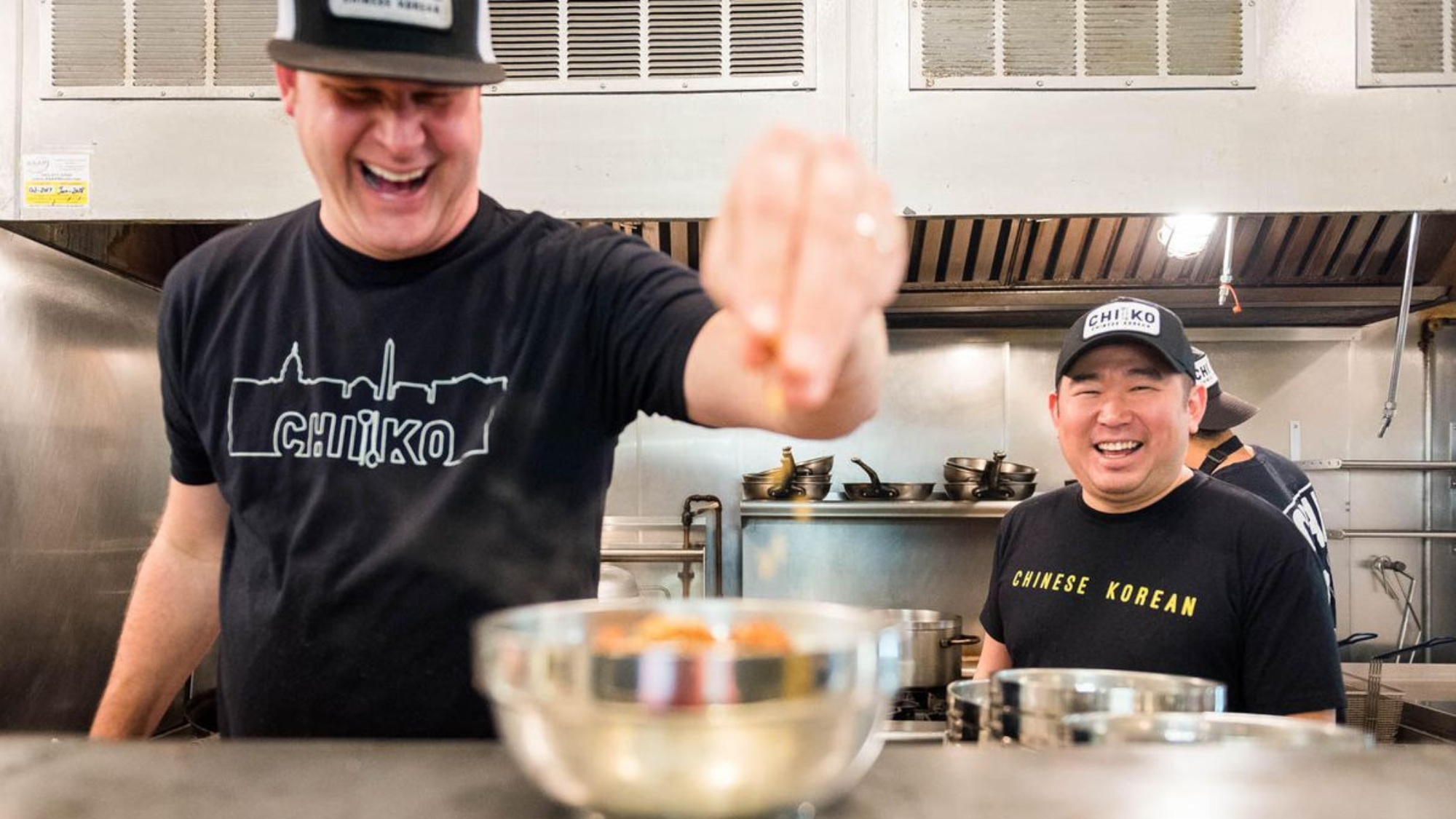 Two smiling men prep ingredients in a restaurant kitchen