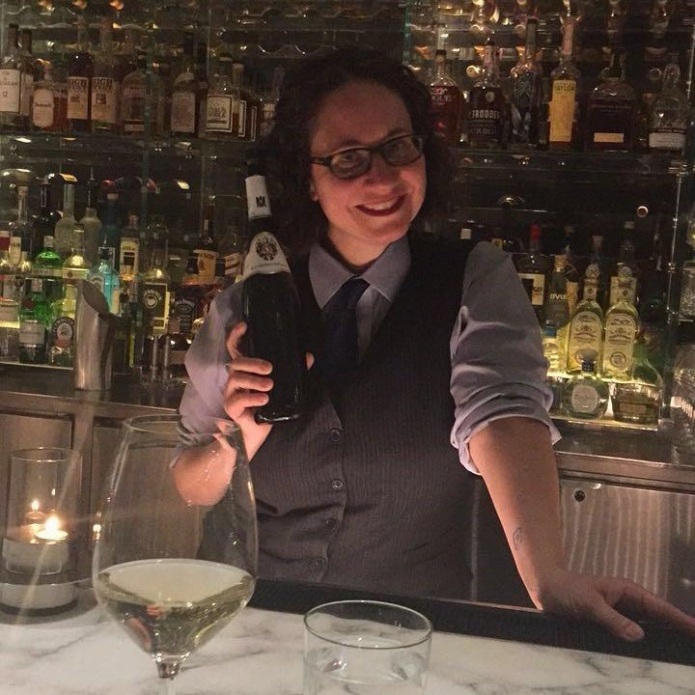 Pamela Vachon, the author, stands behind a bar and holds a bottle of wine