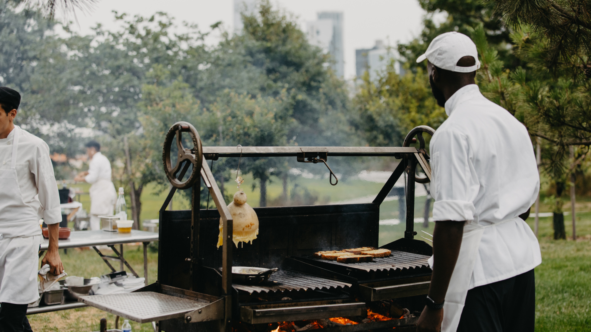 Chefs cooking outdoor at a grill with the Manhattan skyline within view