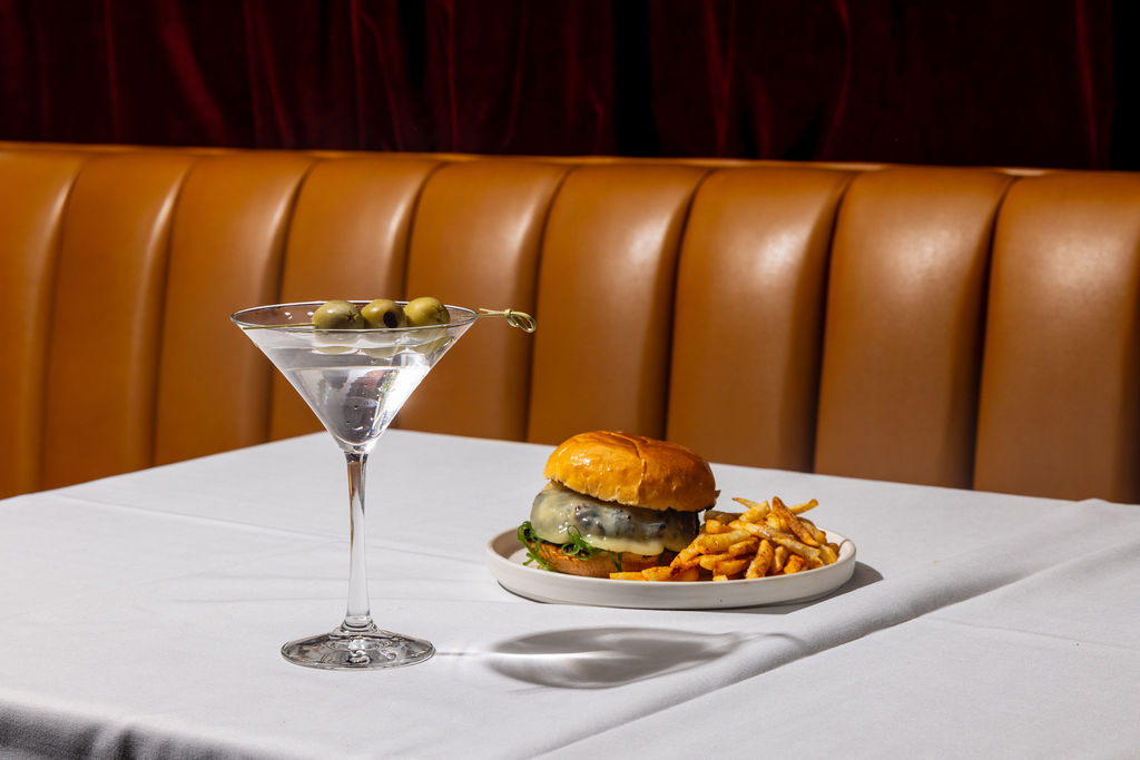 Hamburger and fries sitting on table along with a martini