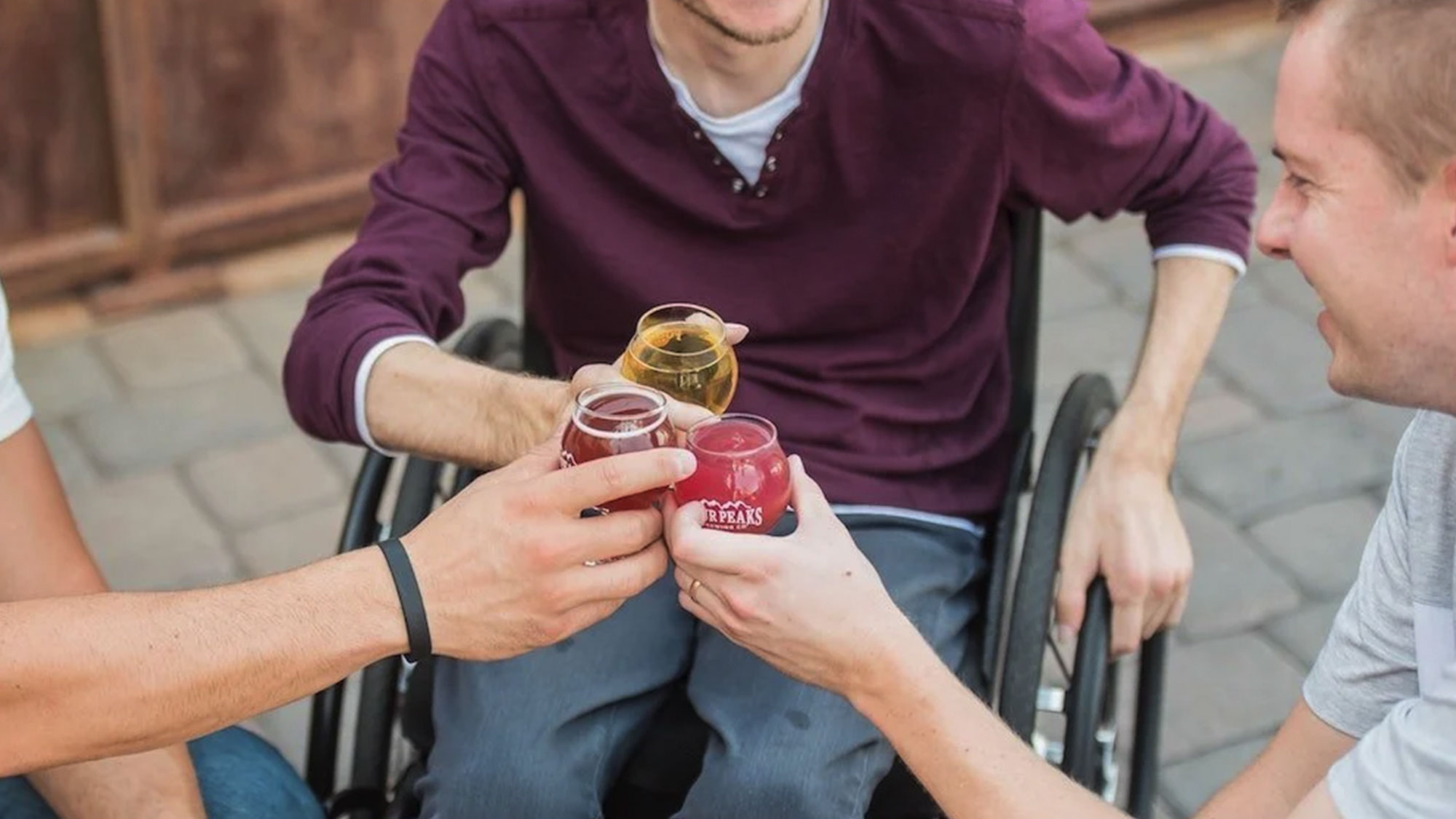 A man in a wheelchair clinks his full glass with two other men