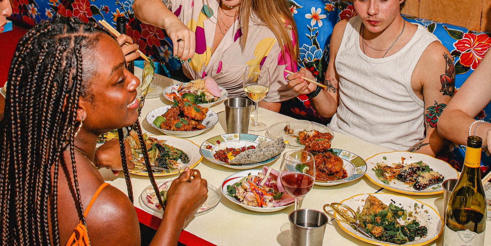 group of people eating at a table with chopsticks while having a glass of wine
