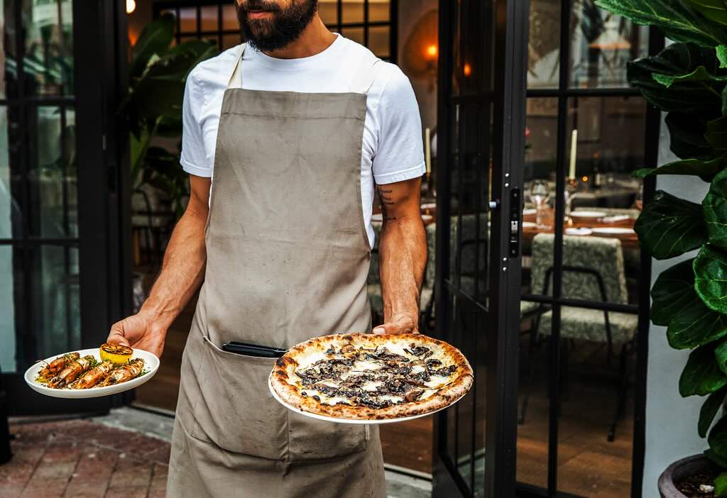 server in apron carrying a pizza and prawns
