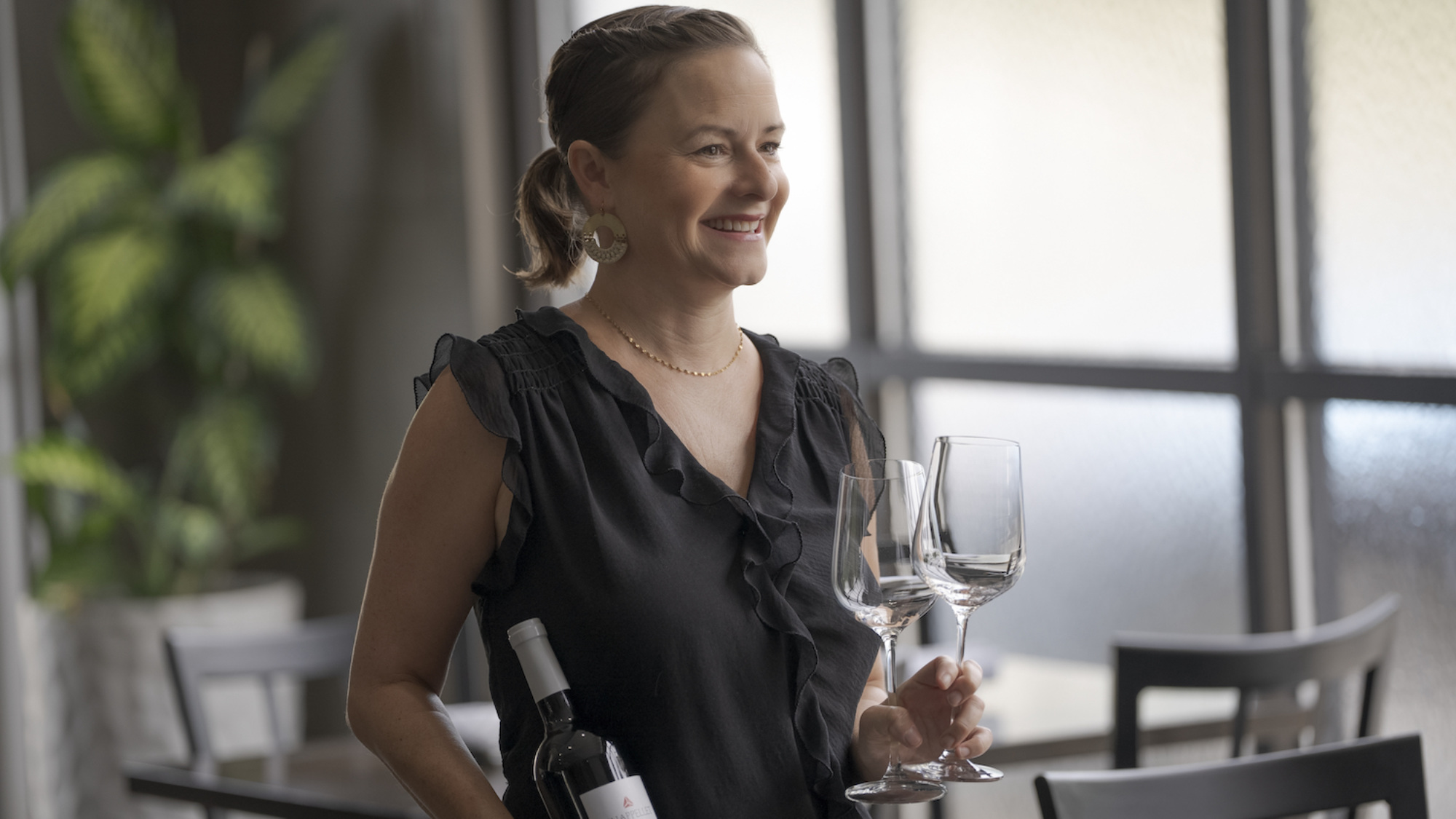 image of server, Rachel Wilson holding a bottle of wine and two wine glasses at 1618 West, in Greensboro, North Carolina