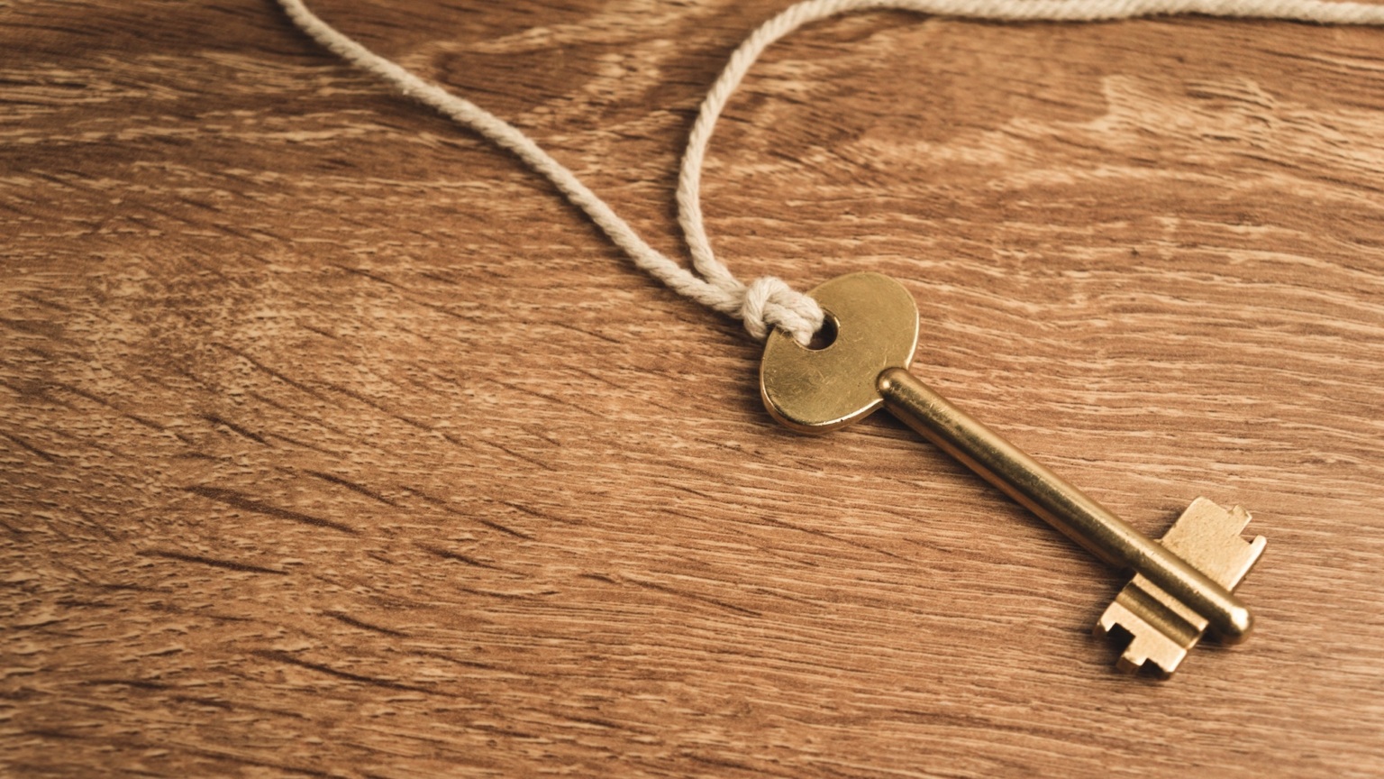 A brass key on a white string lies on a wooden surface.