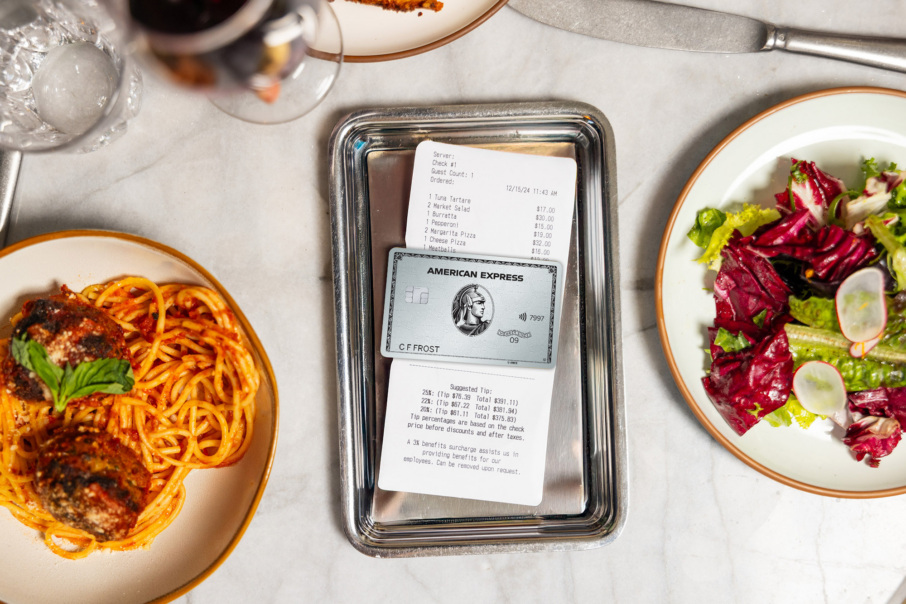 A tablescape with an American Express Platinum Card in a bill tray and plates of food on either side.