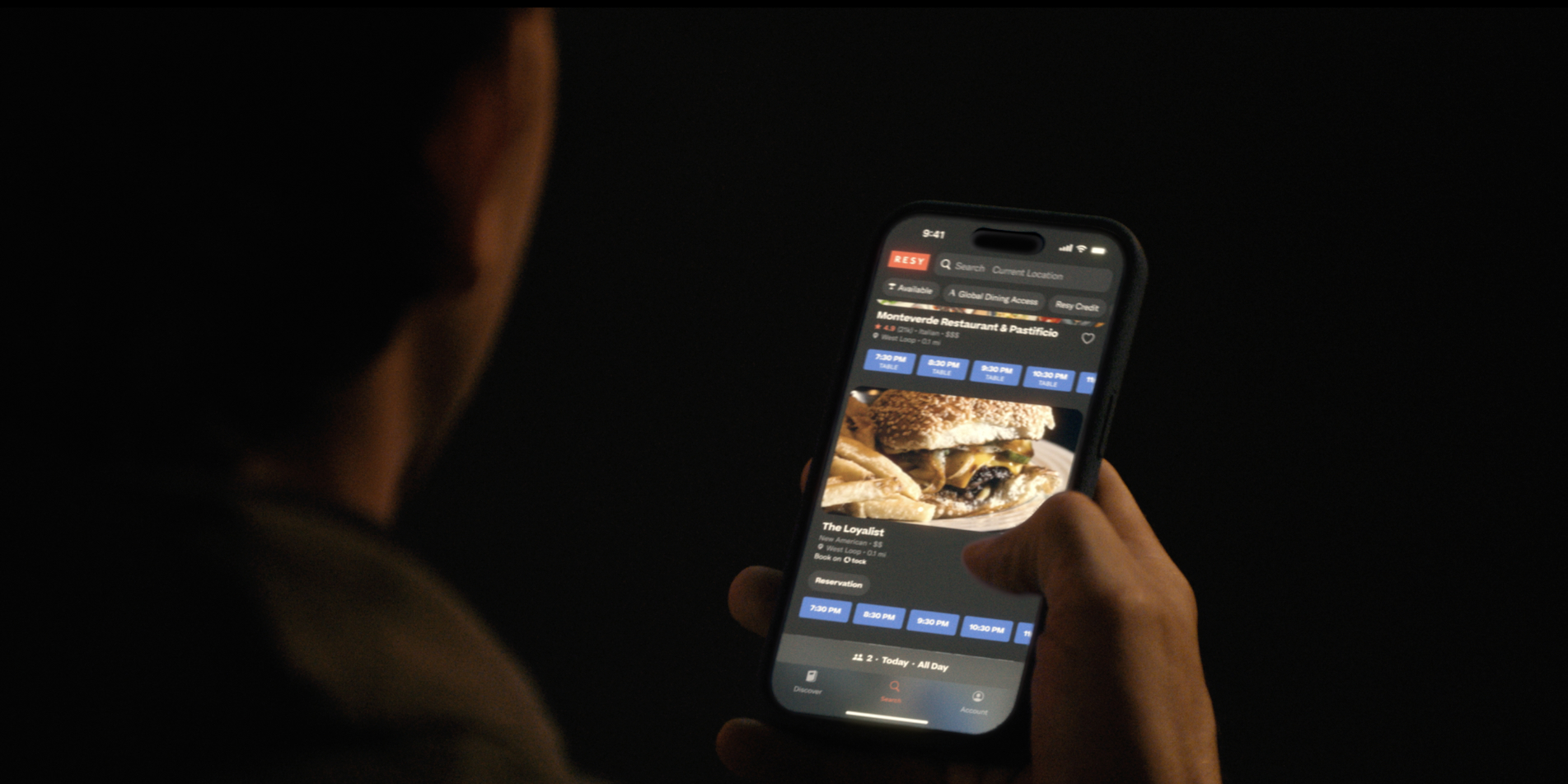 A man scrolls through reservation options on the Resy app on a mobile phone