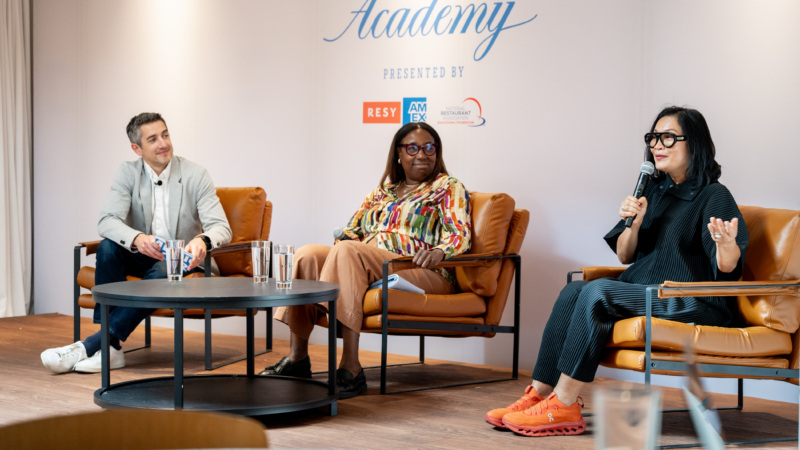 Three individuals, a man and two bespectacled women, speak on a panel.